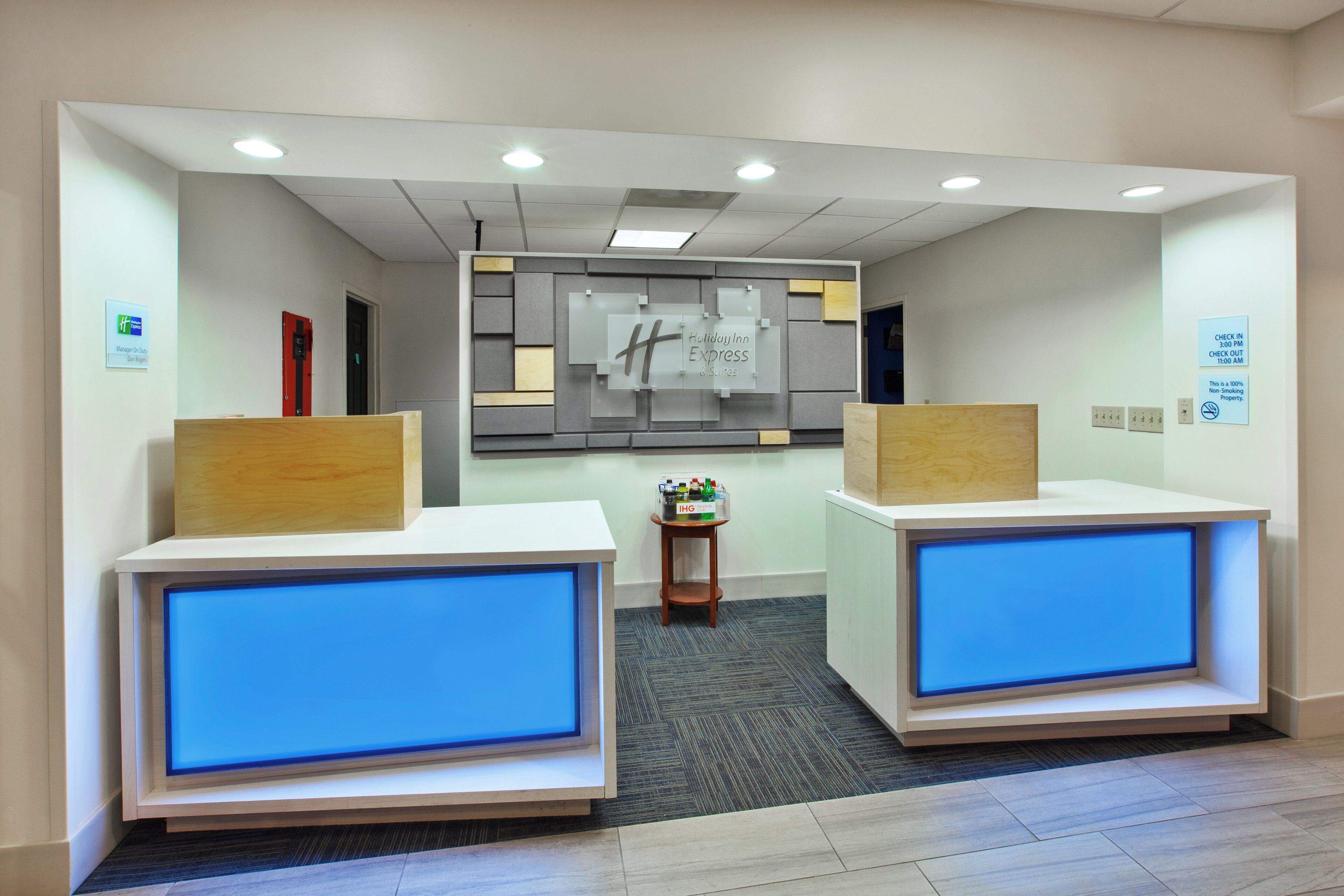 A hotel reception area with two reception desks, a wall-mounted sign, and a small table with a fruit display.