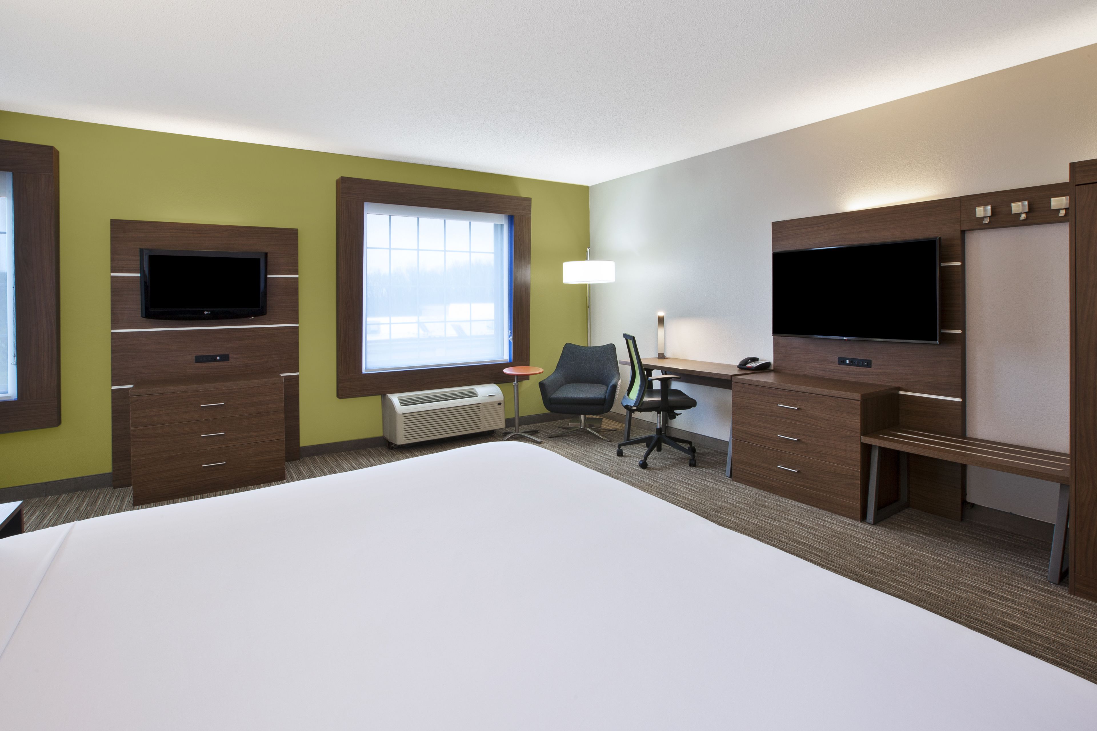 A hotel room with a bed, desk, two TVs, a chair, and a lamp.