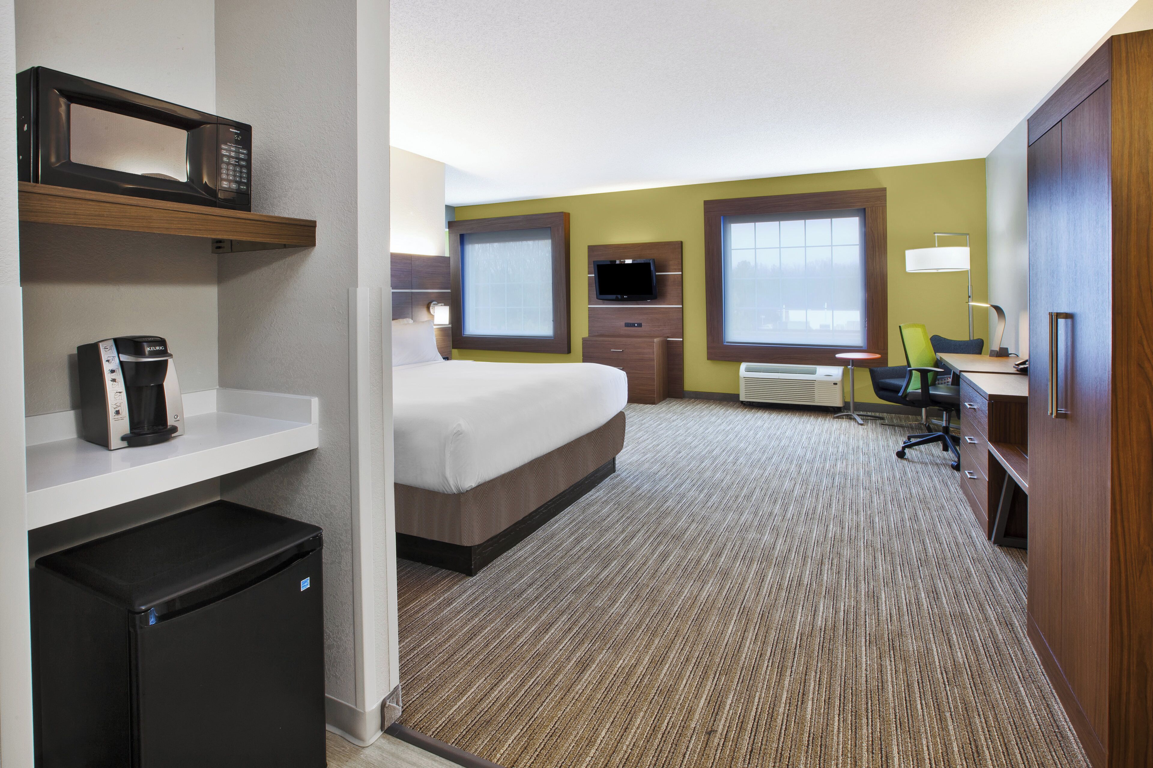 A hotel room with a bed, a desk, a chair, a TV, a coffee machine, and a mini-fridge.