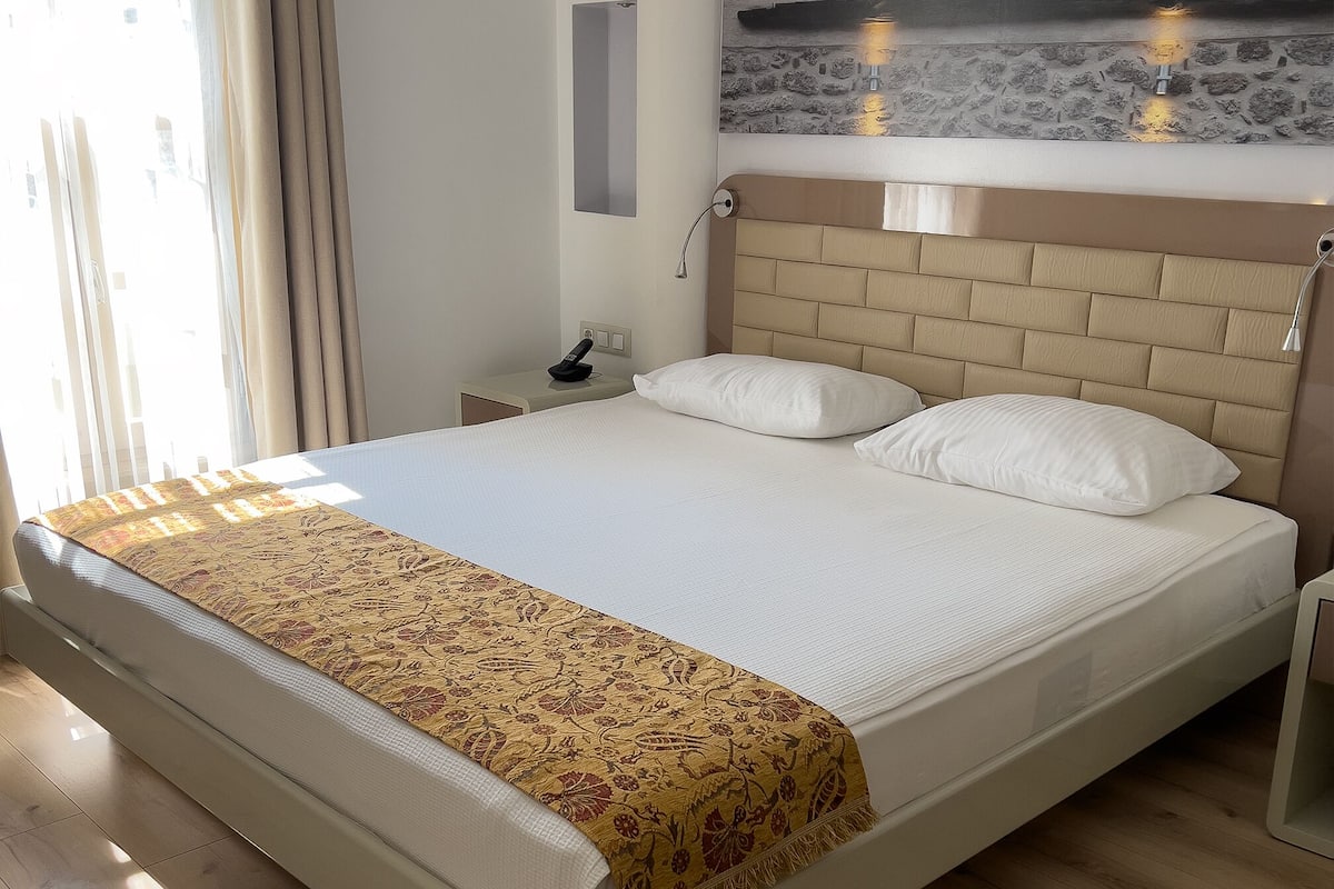A neatly made bed with a patterned throw, a bedside table with a lamp, and a wall-mounted light fixture.