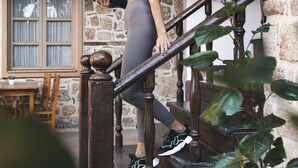 A person on a wooden staircase with a yoga mat, a stone wall, and a window with curtains. - Puding Hotel (Antalya)
