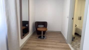 Un pasillo estrecho con suelo de madera, una silla marrón oscuro y una mesa redonda, y un espejo grande en la pared izquierda.