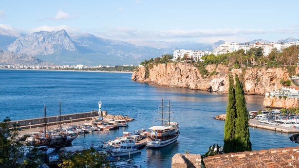 A coastal marina with boats, a lighthouse, and buildings on a cliff. - Puding Hotel (Antalya)