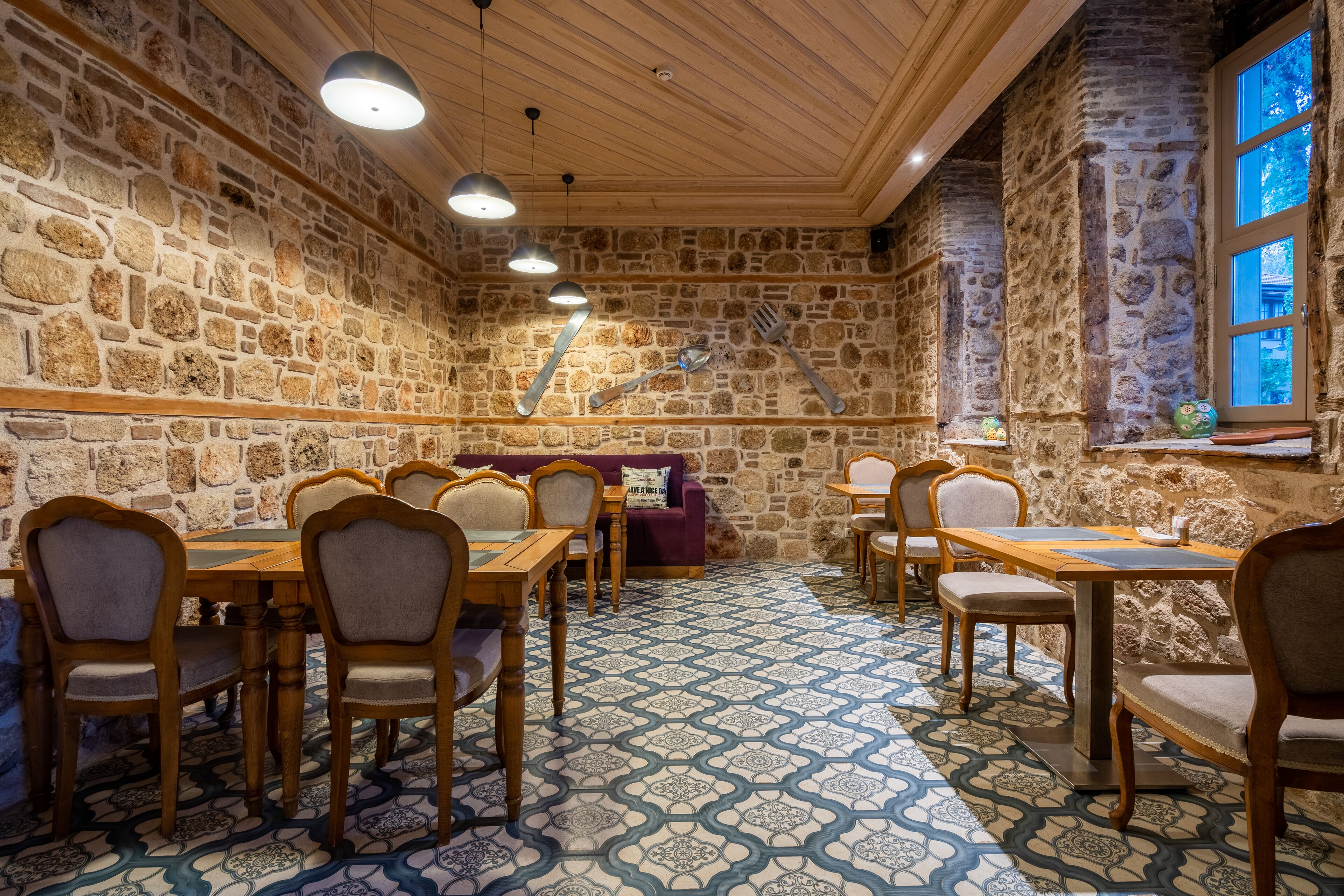 A rustic dining area with stone walls, wooden furniture, and patterned floor tiles.