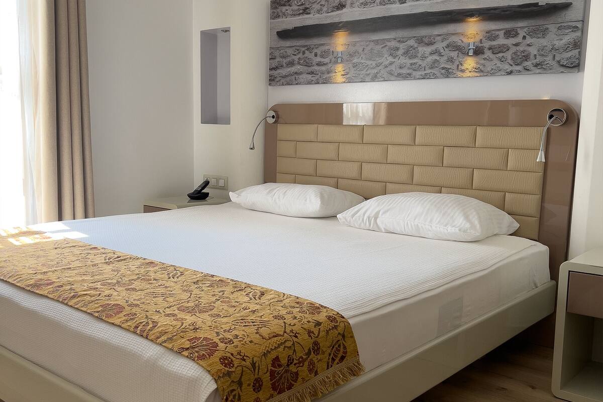 A hotel room with a bed, a nightstand, a wall-mounted light, and a decorative wall piece.