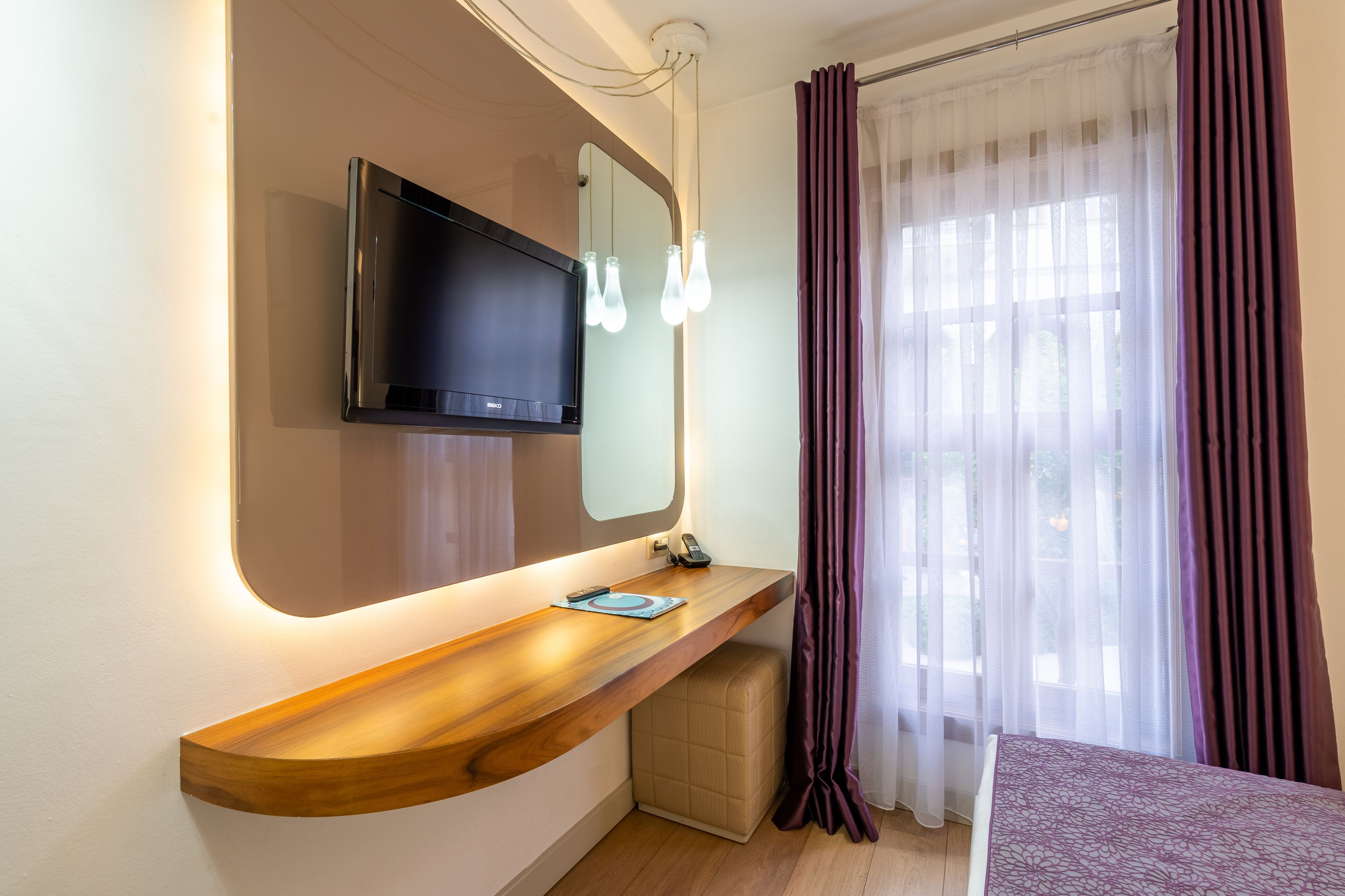 Een moderne badkamer met een houten wastafelmeubel, een tv aan de muur en een grote spiegel.