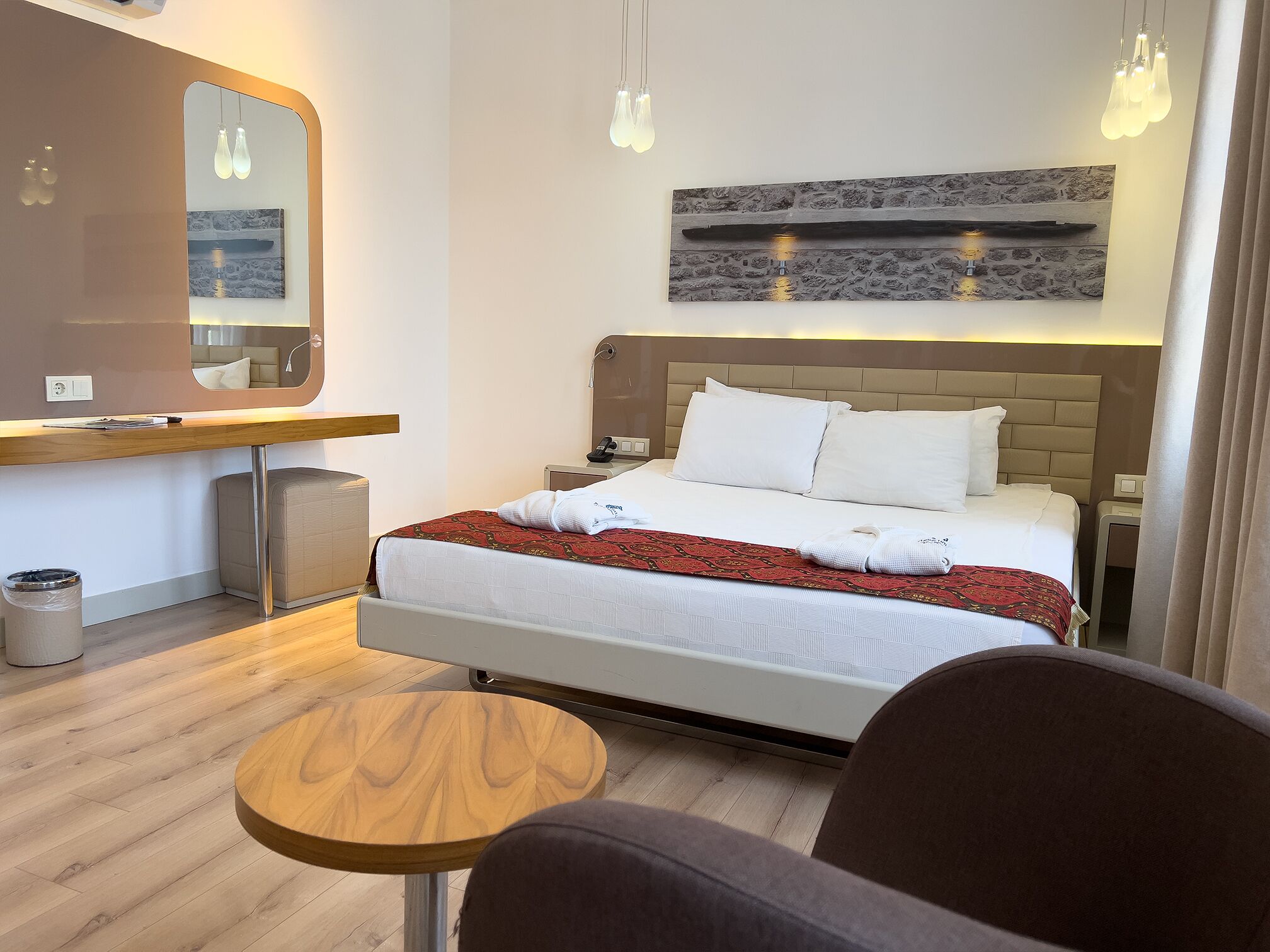 A hotel room with a bed, bedside table, mirror, and a small round table.