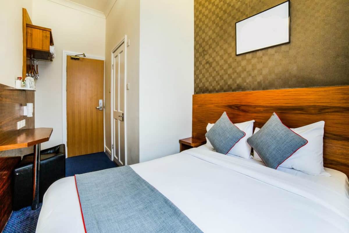 Una habitación de hotel con cama, mesitas de noche, escritorio y puerta.