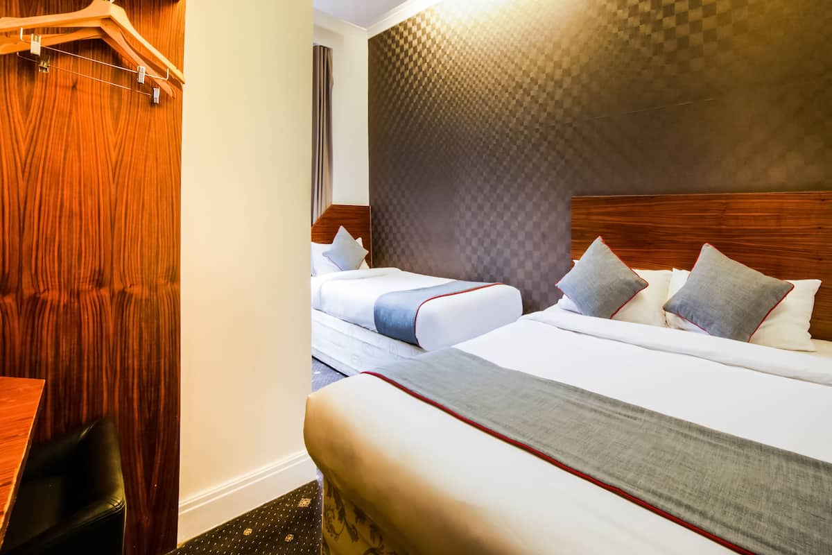 Habitación de hotel con dos camas, cabeceros de madera, pared a cuadros y un perchero.