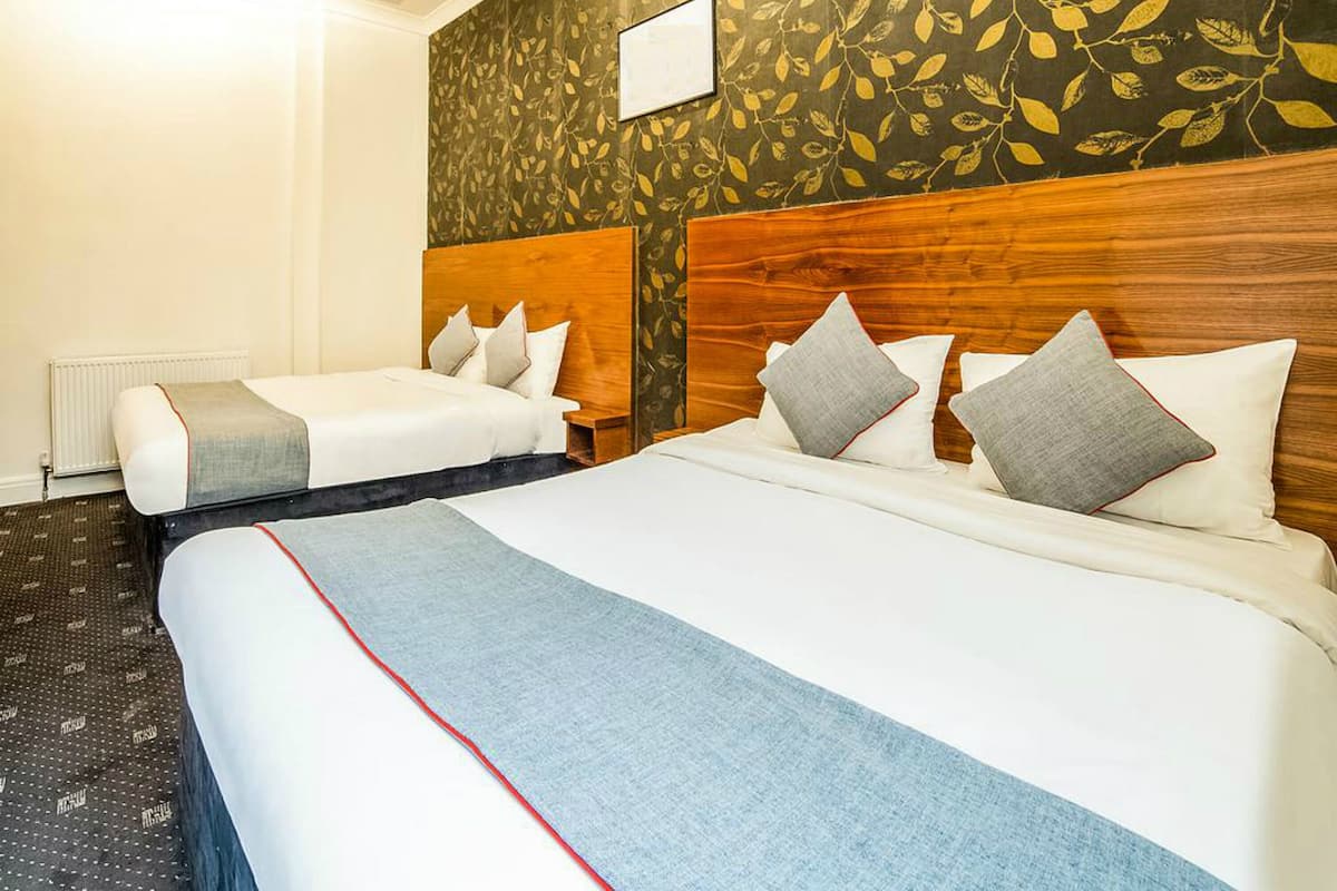 Habitación de hotel con dos camas, un cabecero de madera, papel tapiz con estampado de hojas y un radiador.