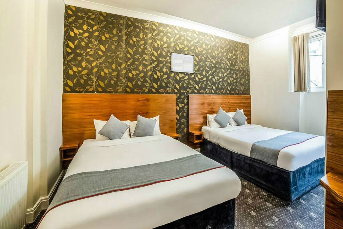 Habitación de hotel con dos camas, cabecero de madera, pared con diseño y una ventana con cortinas.
