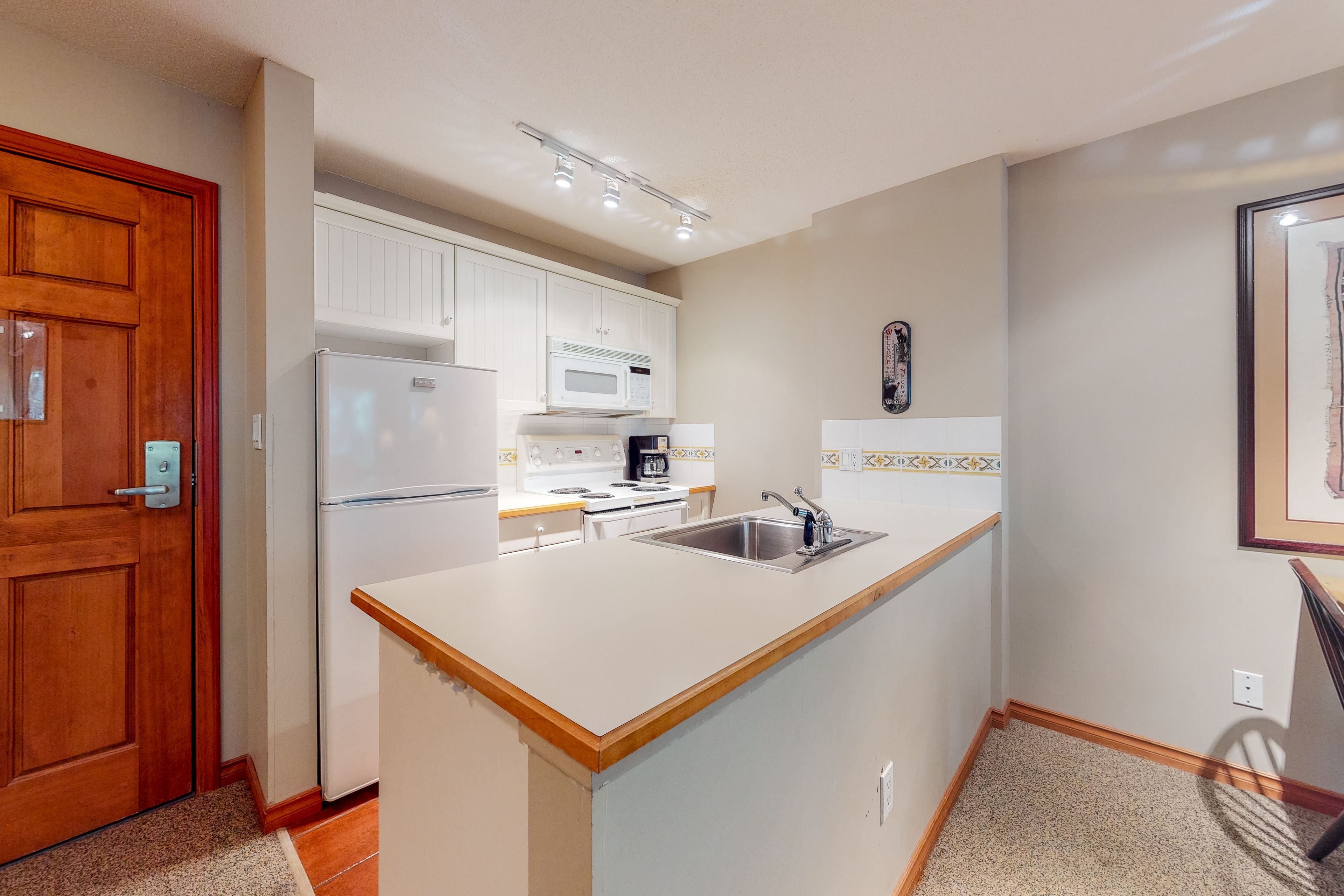 A compact kitchen with white cabinetry, a built-in microwave, a stove, and a sink.