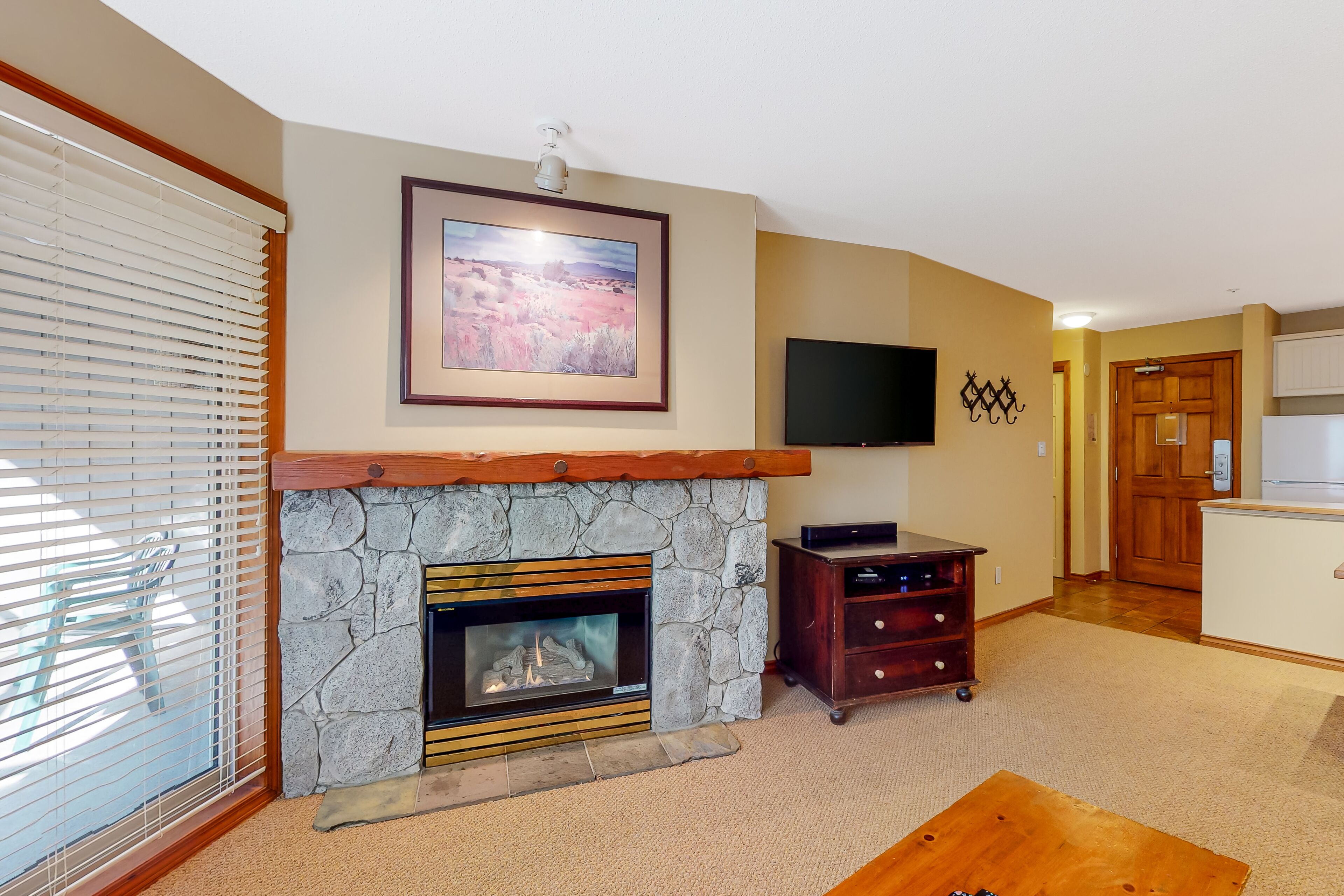 A living room with a stone fireplace, a flat-screen TV mounted on the wall, and a wooden coffee table.
