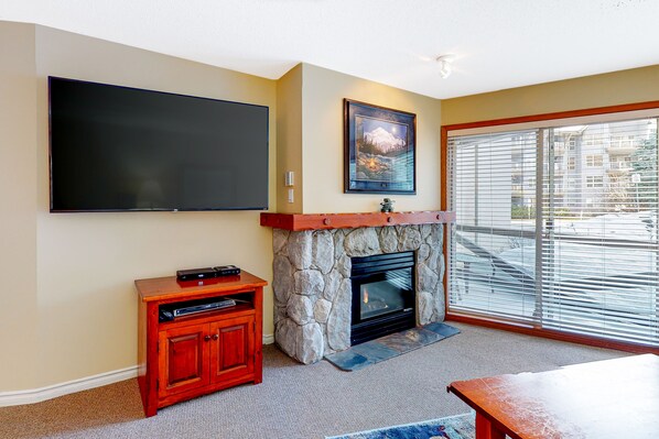 A living room with a stone fireplace, a flat-screen TV mounted on the wall, and a wooden entertainment unit.