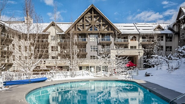 Un resort con piscina, árboles nevados y un edificio de varios pisos con balcones.