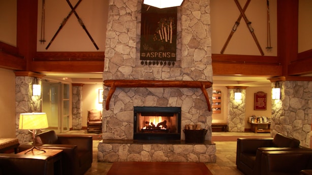 A stone fireplace with a sign above it, surrounded by leather sofas and a wooden table. - Aspens on Blackcomb (Whistler)