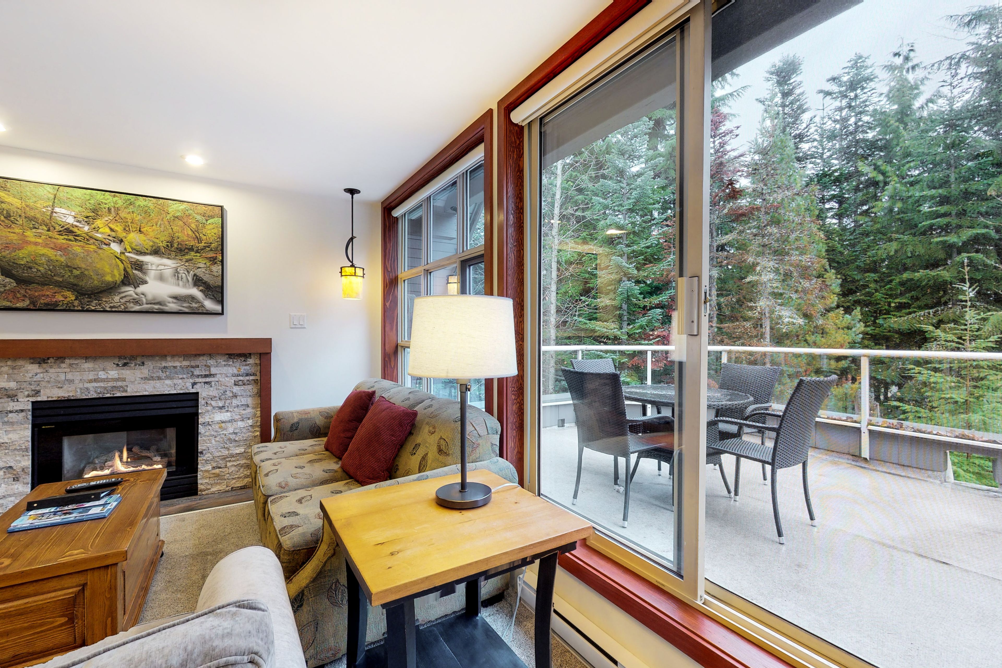 A cozy living room with a fireplace, comfortable seating, a table, and a large window offering a view of the outdoors.