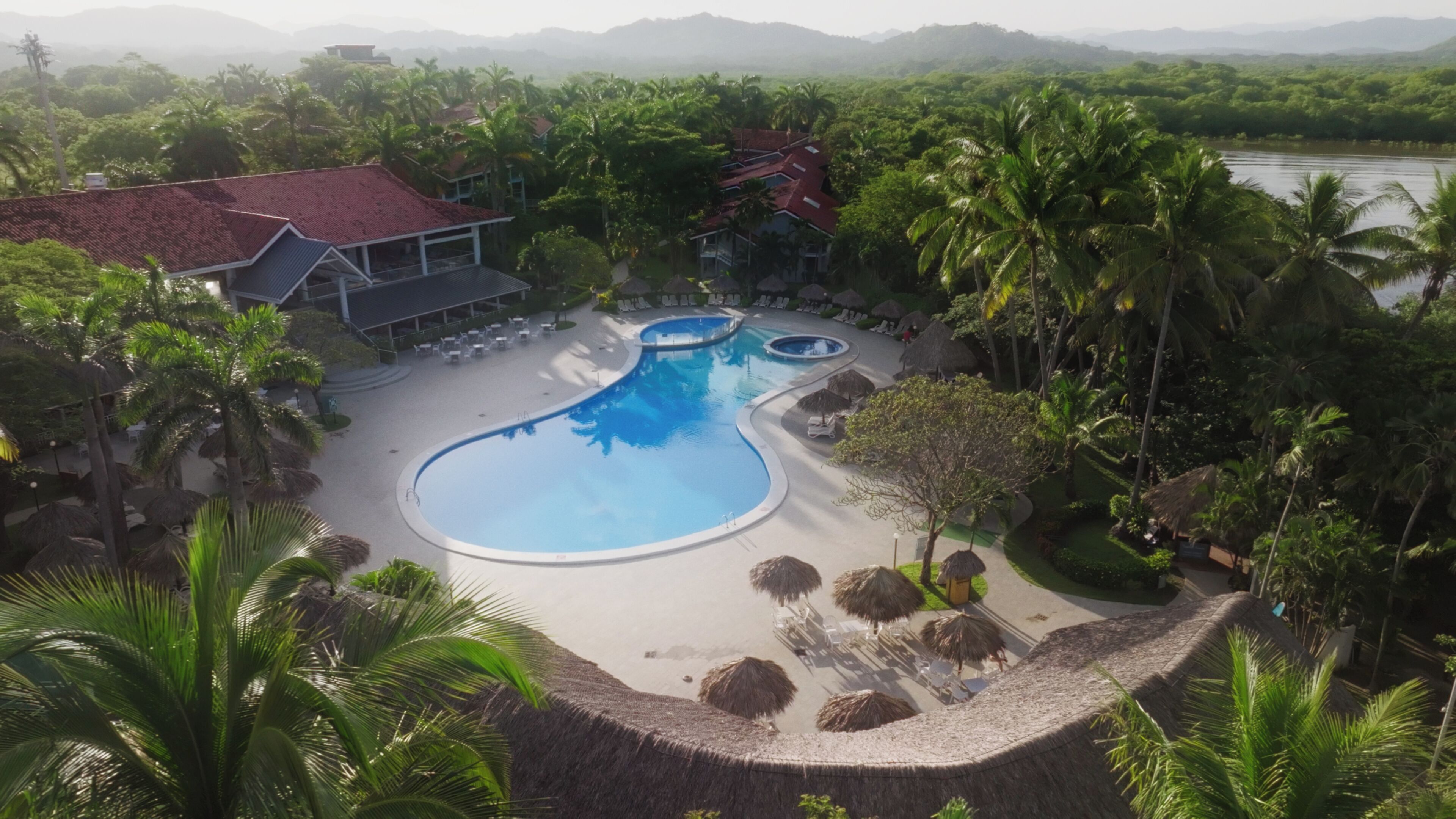 A resort with a large swimming pool, palm trees, and a view of the mountains.