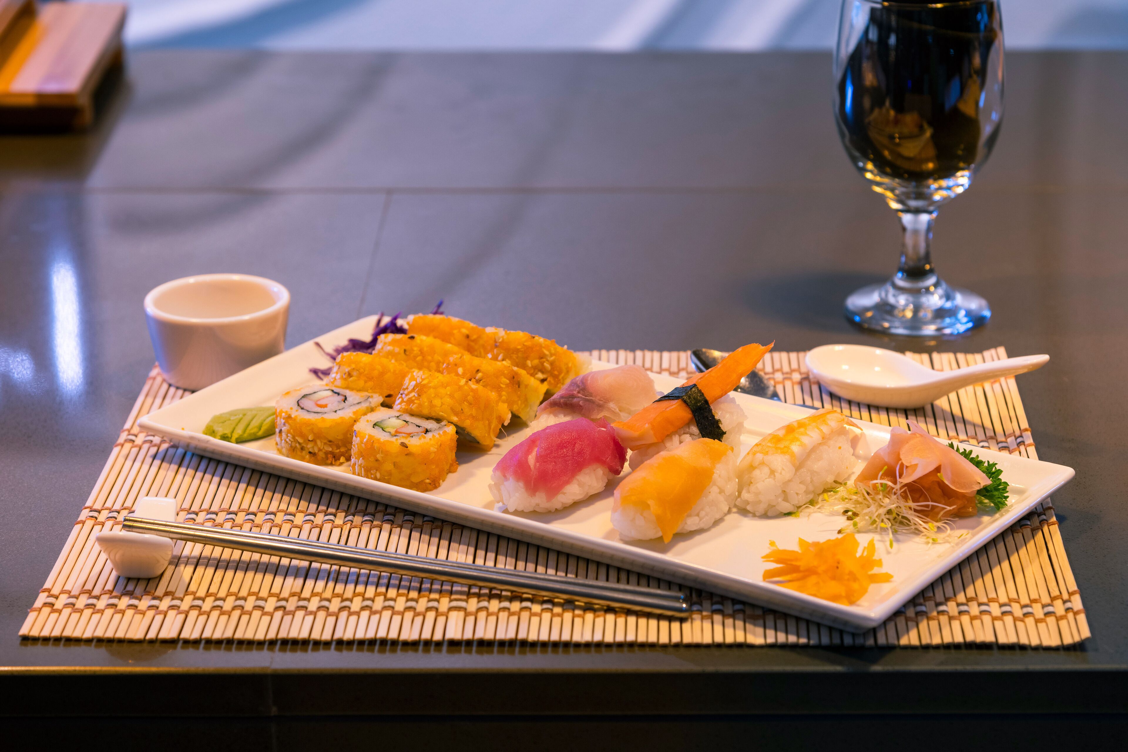 Una bandeja de sushi sobre una mesa, con palillos y una taza pequeña.