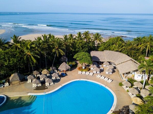 A resort with a swimming pool, lounge chairs, and thatched umbrellas.