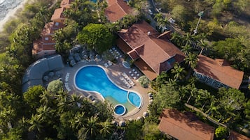 Vista aérea de un complejo turístico con varias edificaciones, una piscina grande y una playa.