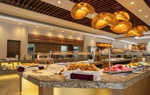 A buffet area with various food items, including pastries and fruits, in a modern setting with wooden ceiling and lighting fixtures.
