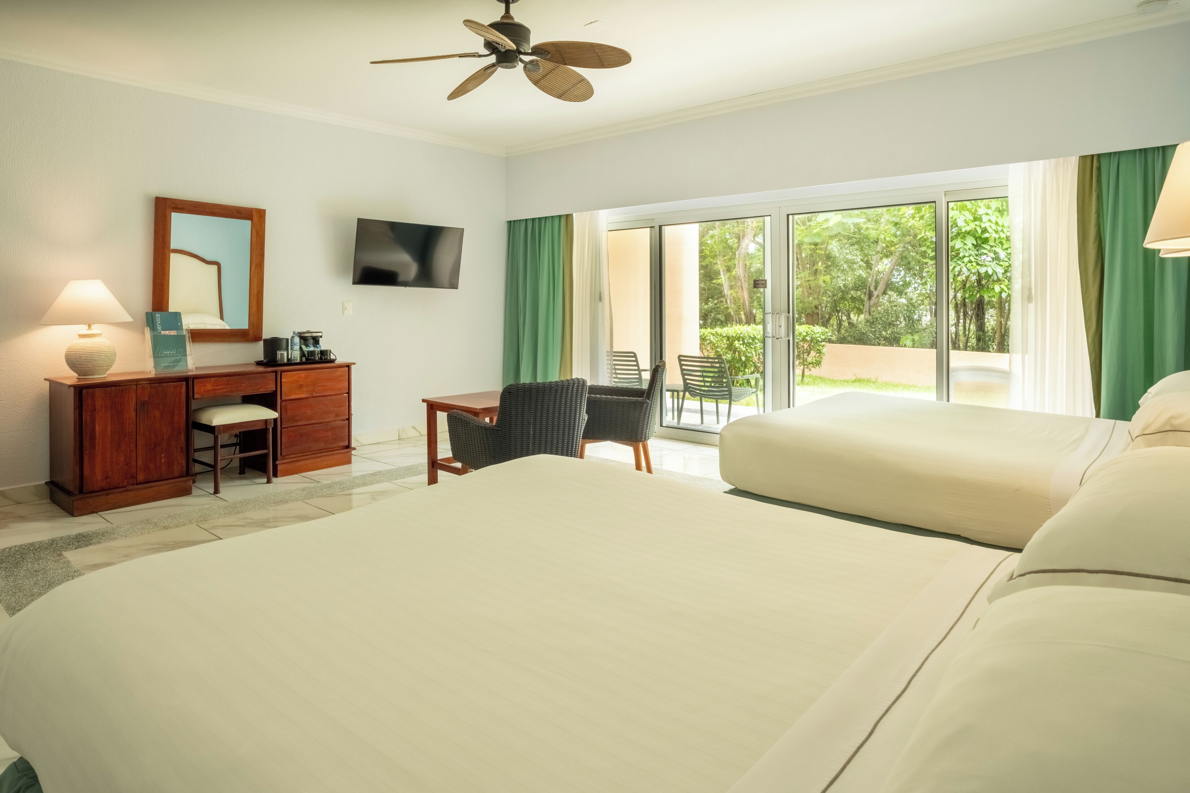 Habitación de hotel con una cama grande, un escritorio con lámpara, una silla, un televisor y un ventanal corredero que da a un balcón.