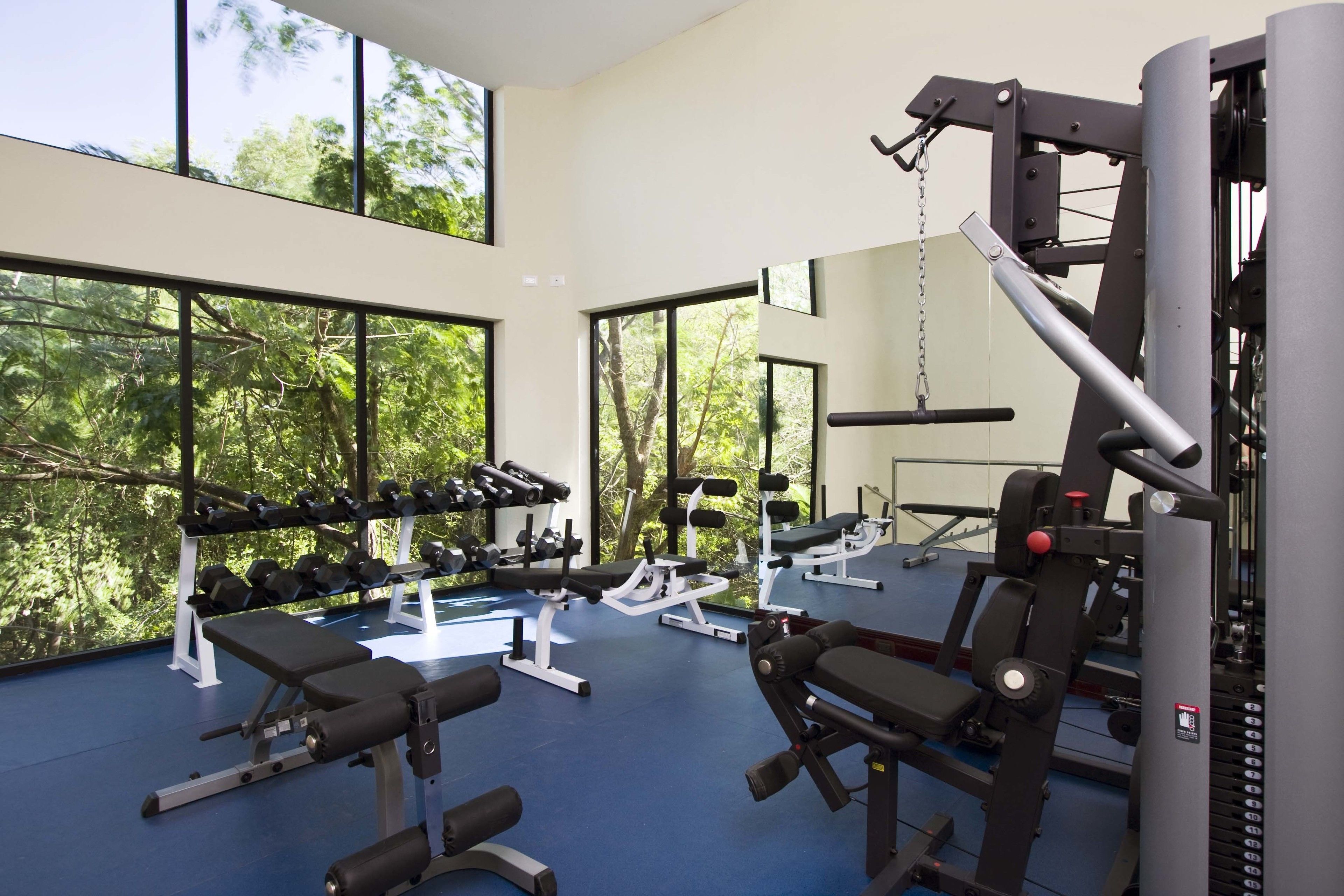 Ett gym med träningsutrustning, stora fönster och ett blått golv.