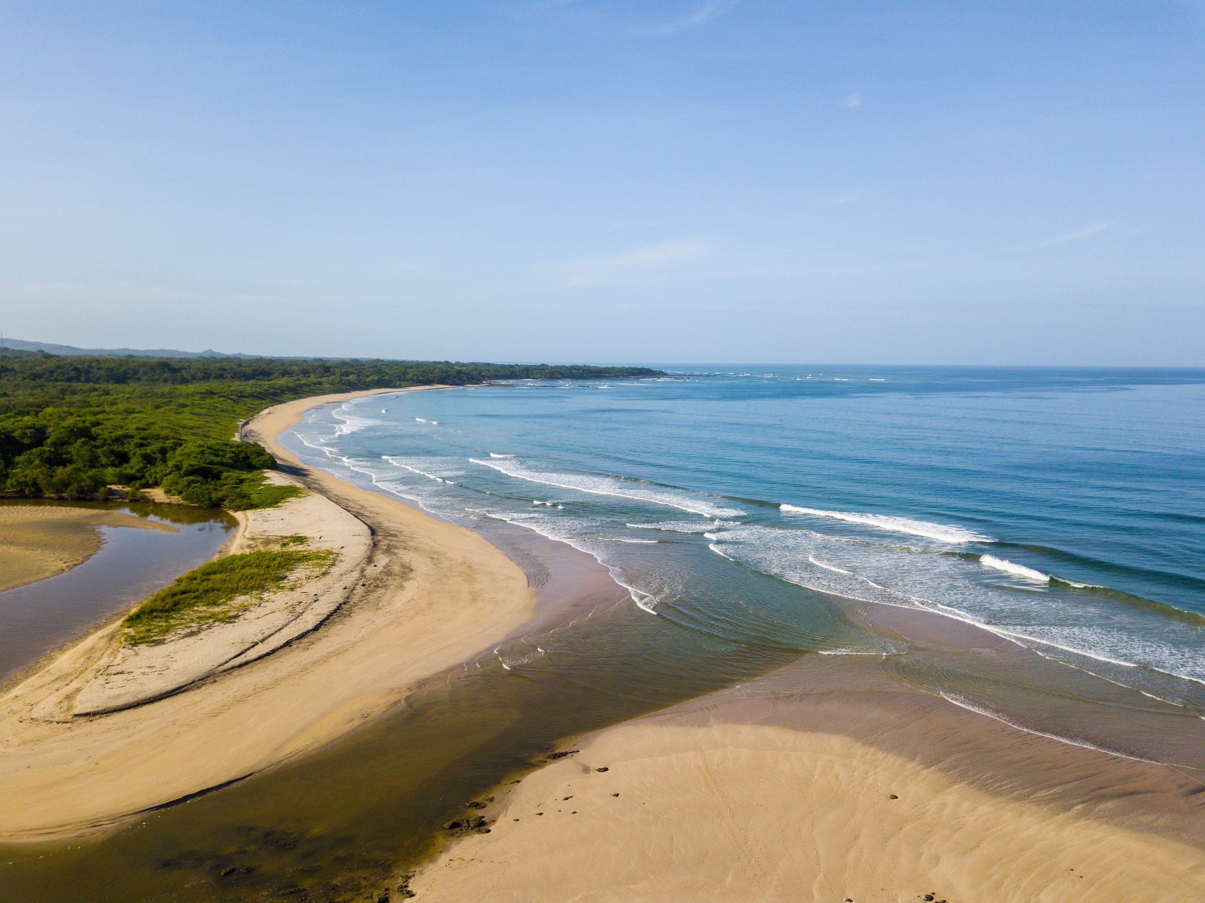 Eine Küstenlandschaft mit Sandstrand, ruhiger See und bewaldetem Hintergrund.