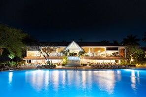 A hotel with a swimming pool, outdoor seating, and a well-lit entrance.