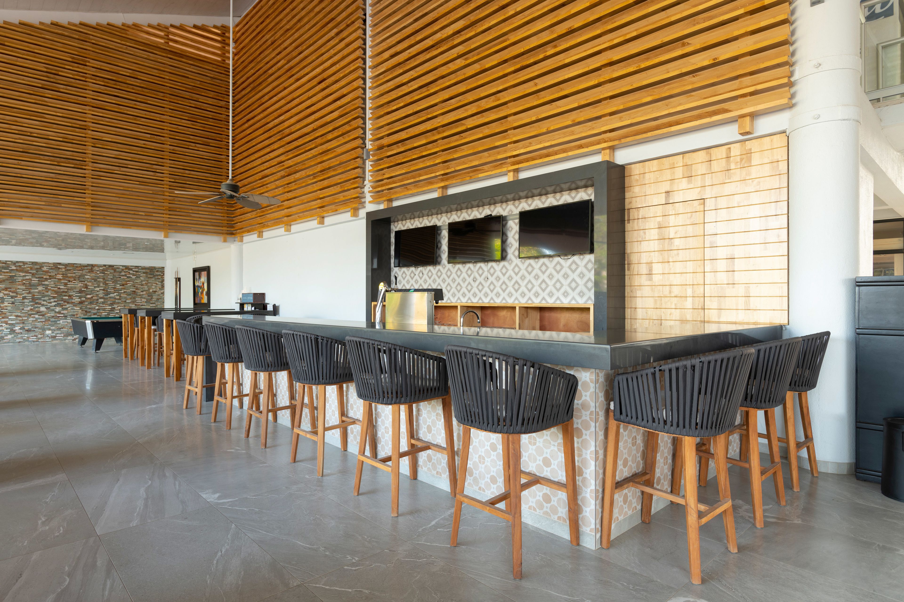 A modern kitchen with a bar area, wooden slatted ceiling, and a stone accent wall.