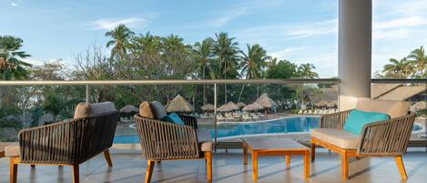 Un balcón con mobiliario de mimbre, piscina y vista a palmeras.