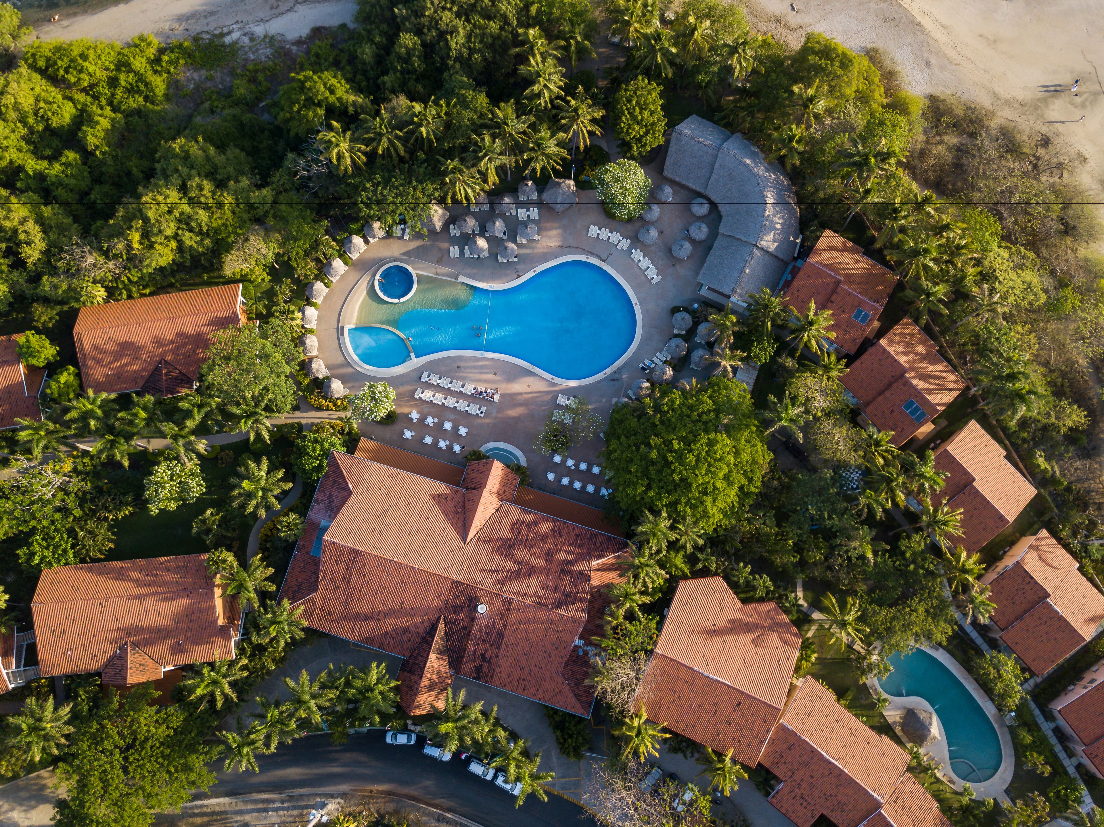 An aerial view of a resort with a large central pool, multiple smaller pools, and numerous sun loungers.