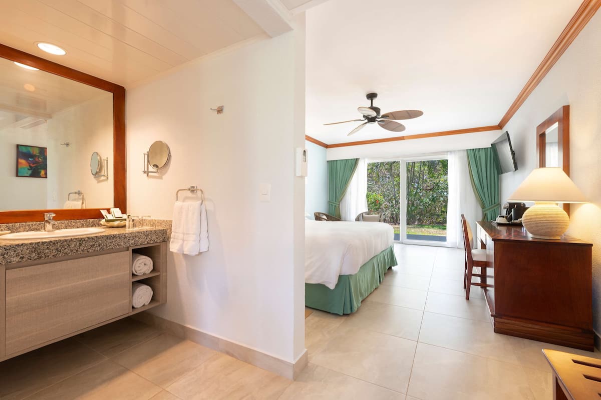 Una habitación de hotel con baño, una cama, un escritorio y un ventilador de techo.