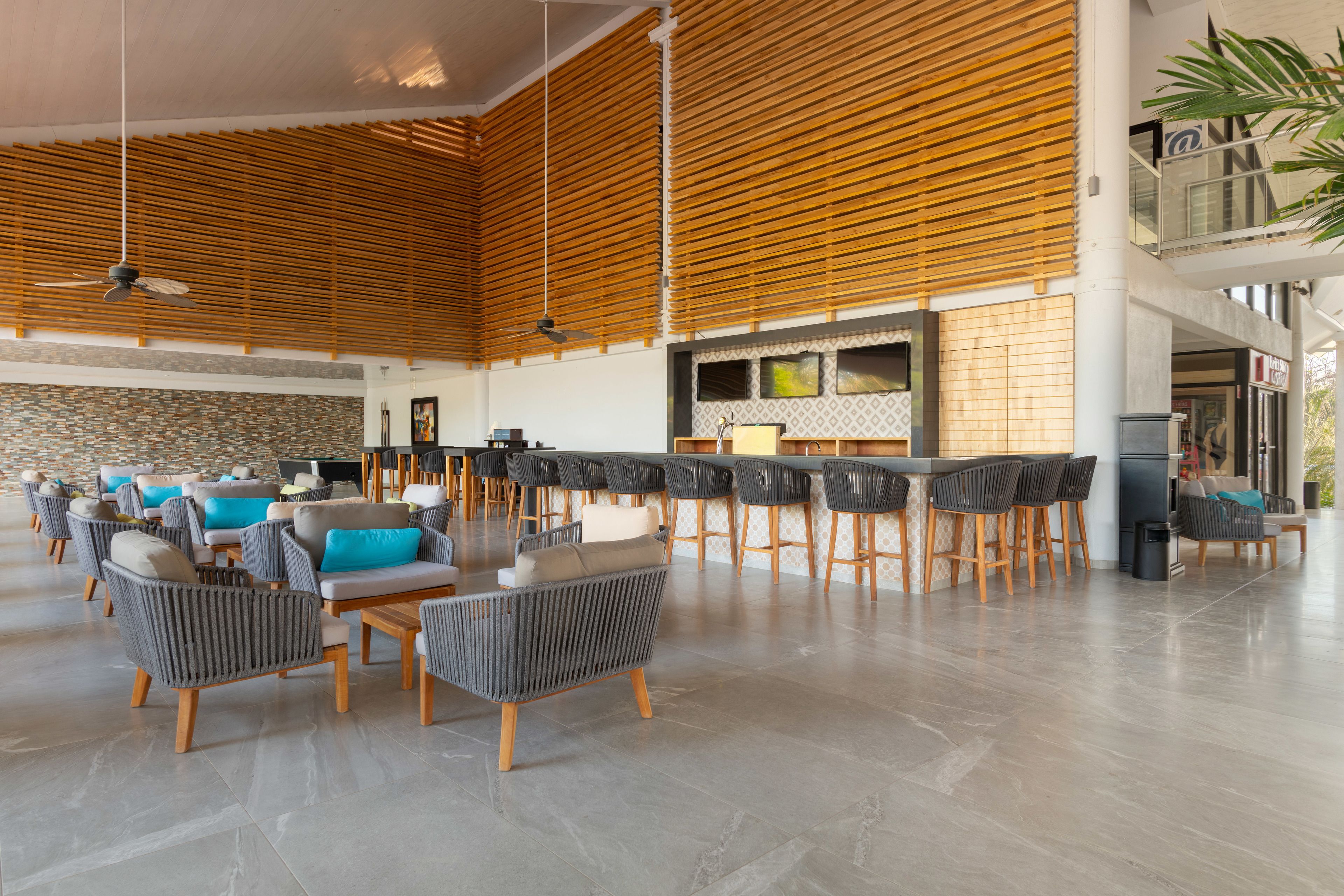 A spacious lobby with high ceilings, wooden slats, and a bar area with stools.