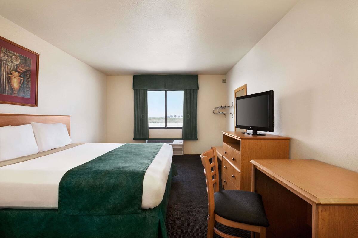 A hotel room with a bed, a desk, a television, and a window with curtains.