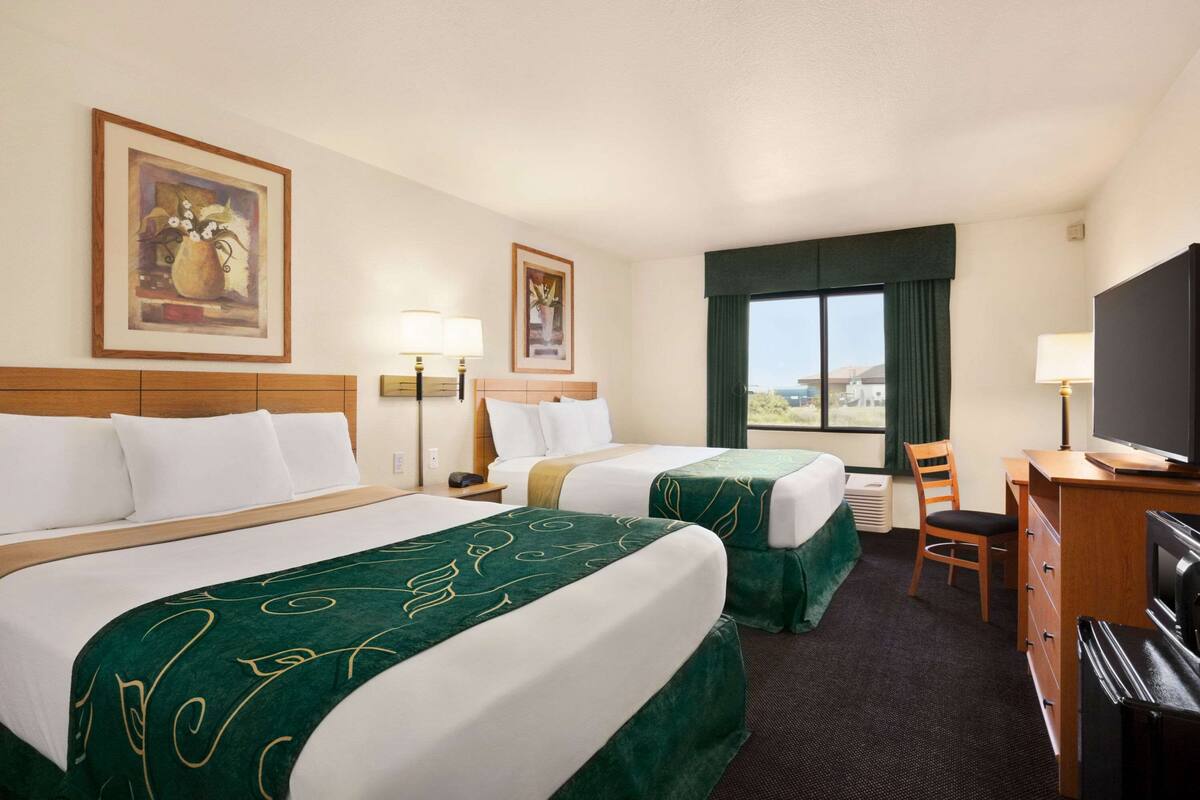 A hotel room with two beds, a desk, a television, and a window with a view.