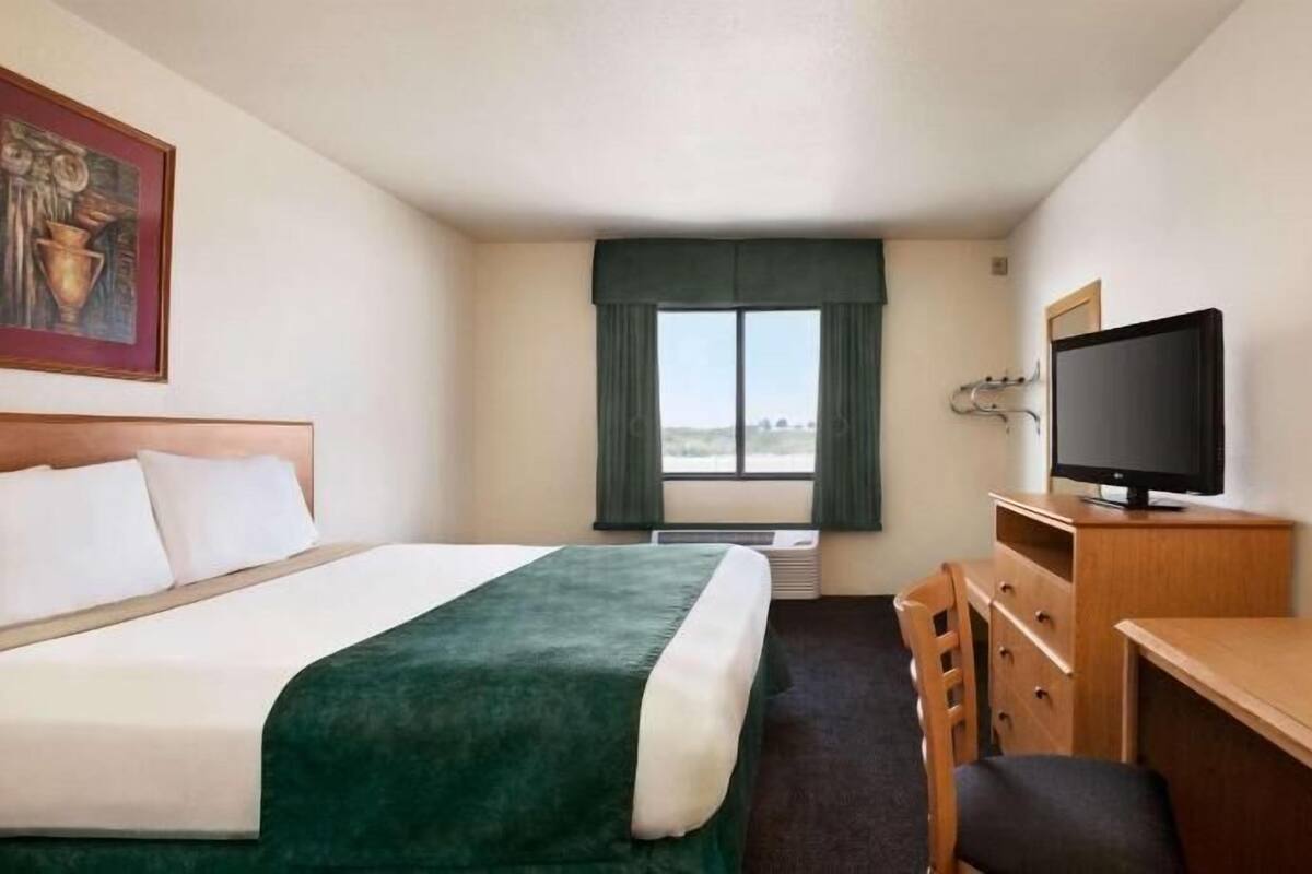 A hotel room with a bed, a desk, a television, and a window with curtains.