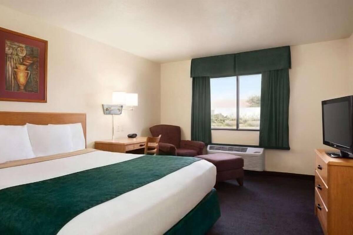 A hotel room with a large bed, a desk, a chair, a television, and a window with curtains.