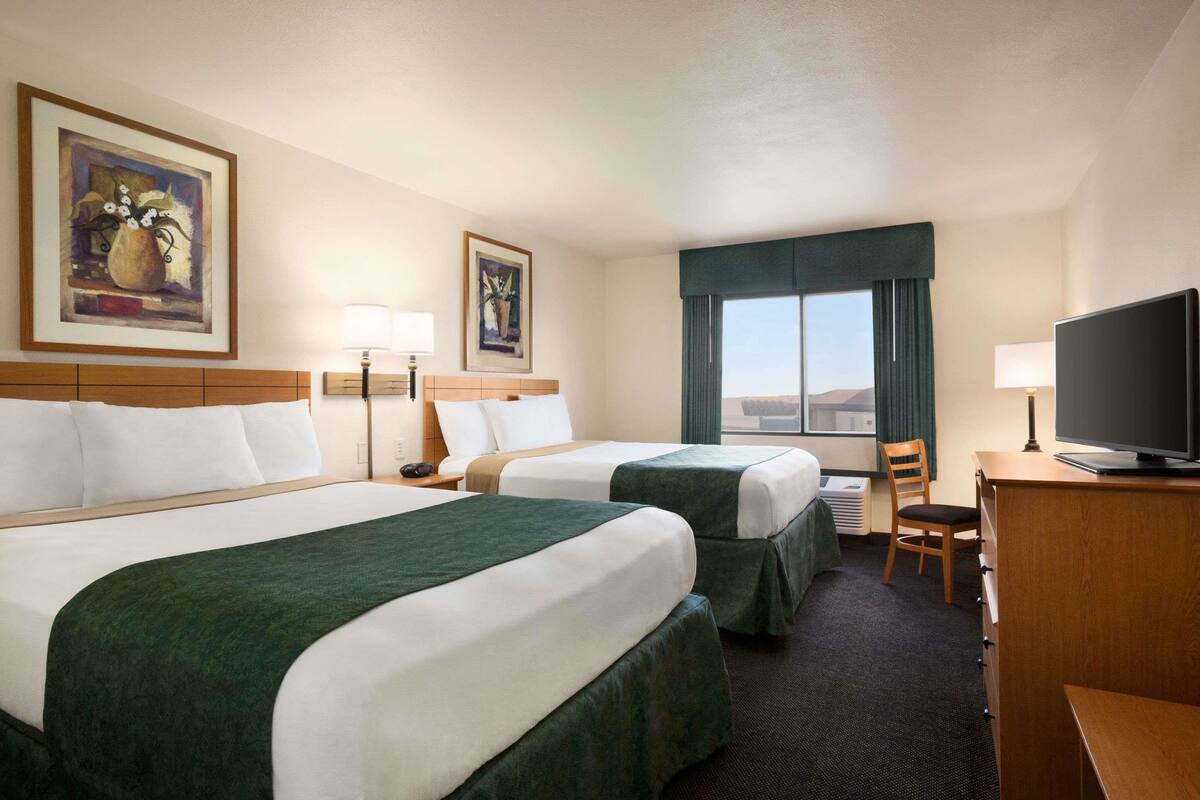 A hotel room with two beds, a desk with a television, a chair, and a window with curtains.