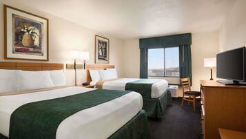 A hotel room with two beds, a desk with a television, a chair, and a window with curtains.