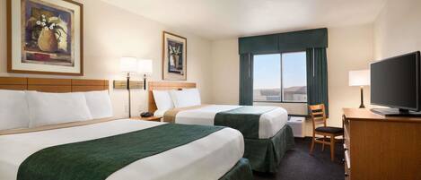 A hotel room with two beds, a desk with a television, a chair, and a window with curtains.