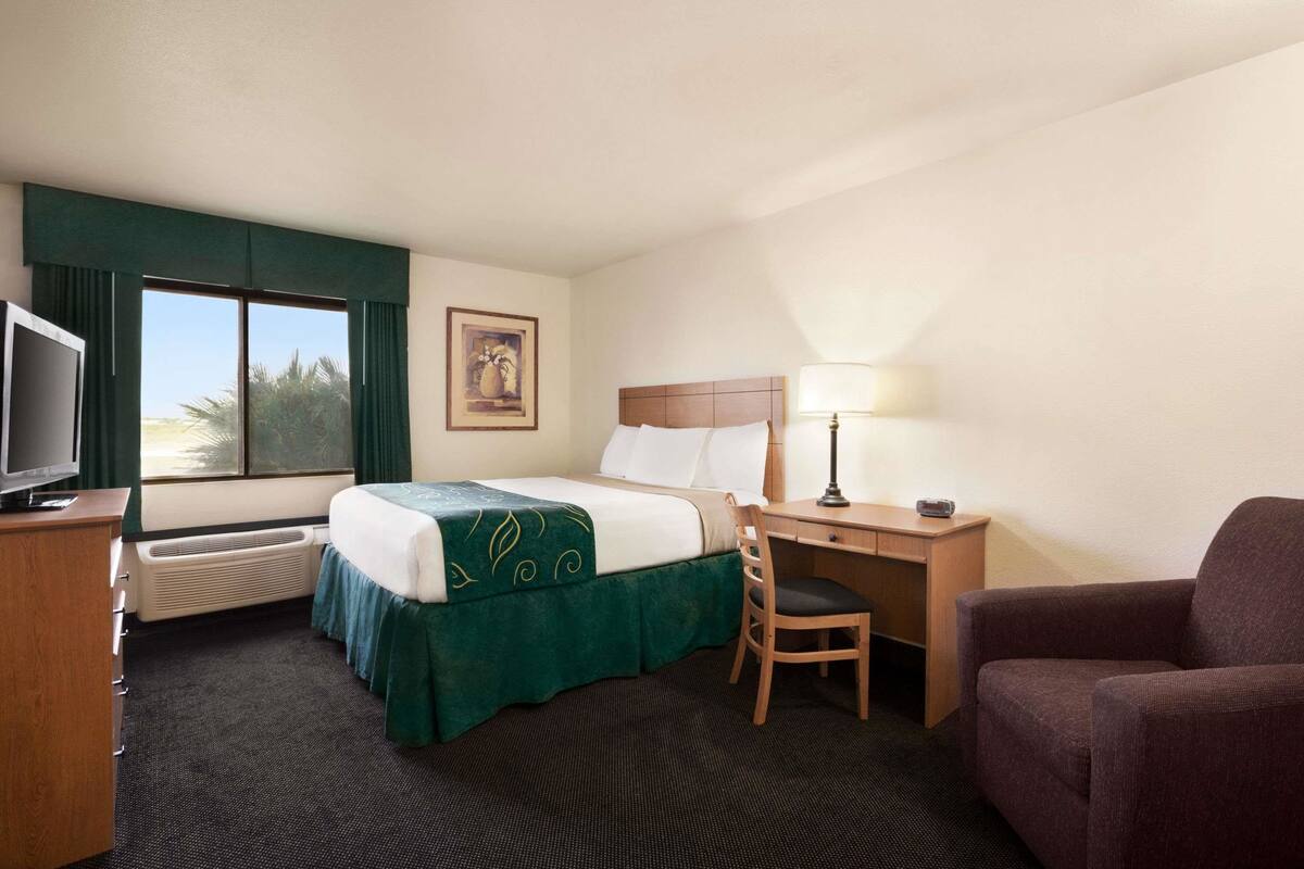 A hotel room with a bed, a desk, a chair, a TV, and a window with curtains.