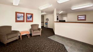 En hotelllobby med två fåtöljer, ett litet bord, en receptionsdisk och inramade tavlor på väggarna.