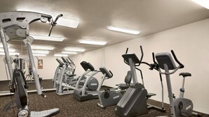 Ett gym med olika träningsmaskiner, heltäckningsmatta på golvet och takbelysning.
