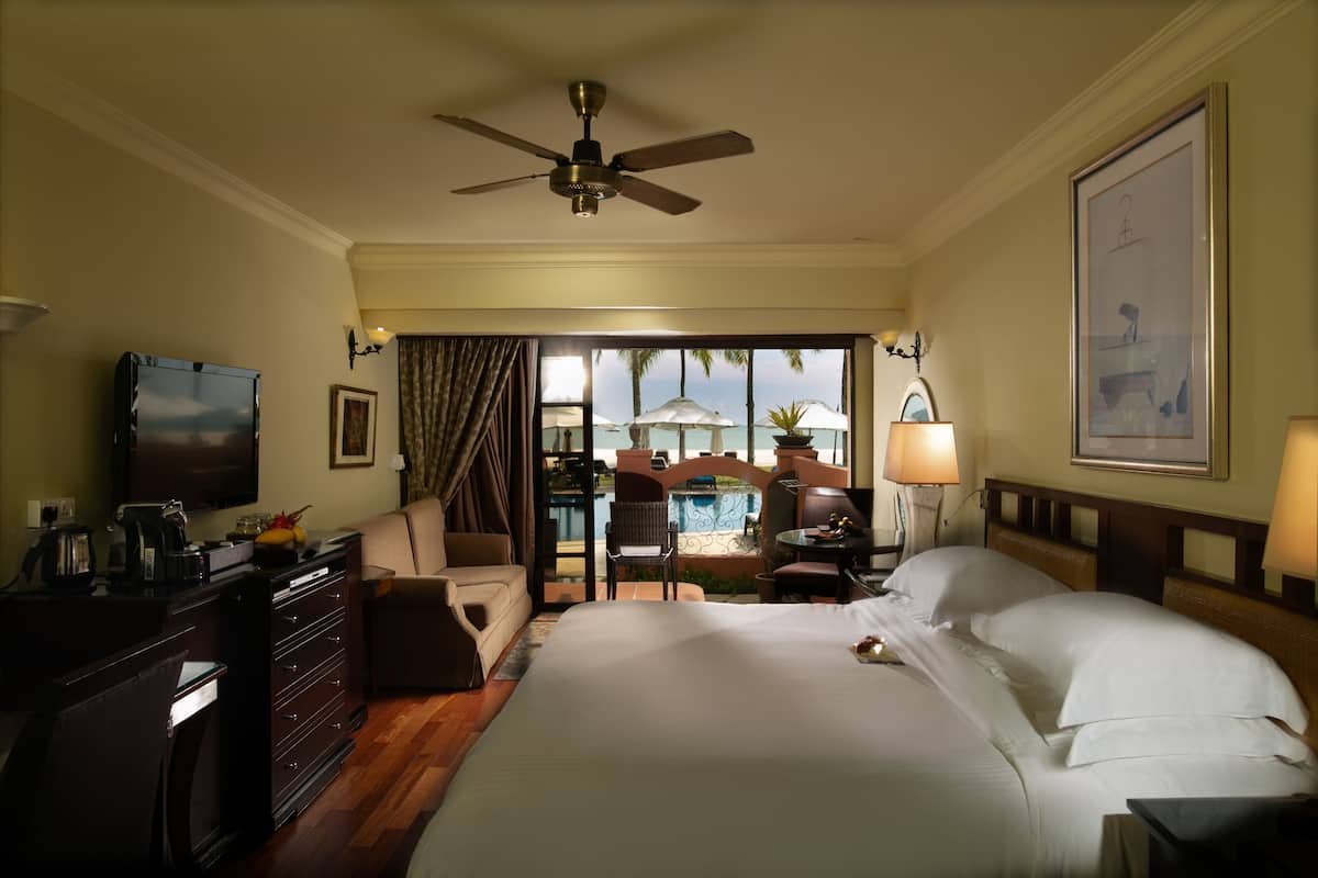 Une chambre d’hôtel équipée d’un lit, d’un bureau, d’une chaise, d’une télévision et offrant une vue sur la plage.