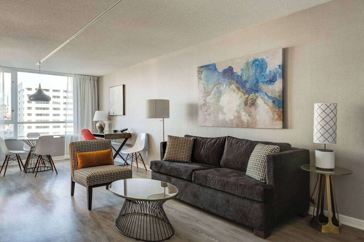 A modern living room with a dark grey sofa, a glass coffee table, and a large abstract painting on the wall.