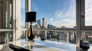 A modern office space with a glass desk, a black lamp, and a view of a cityscape through large windows.