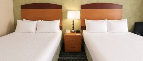 A hotel room with two beds, a nightstand with a lamp, and a telephone.