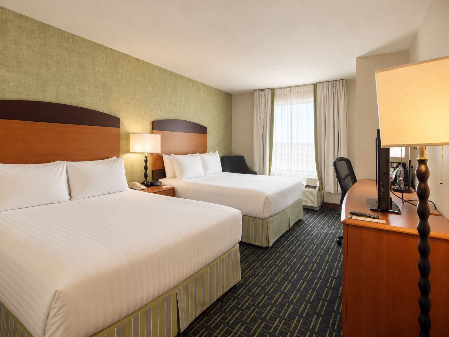 A hotel room with two beds, a desk with a computer, a telephone, and a lamp.